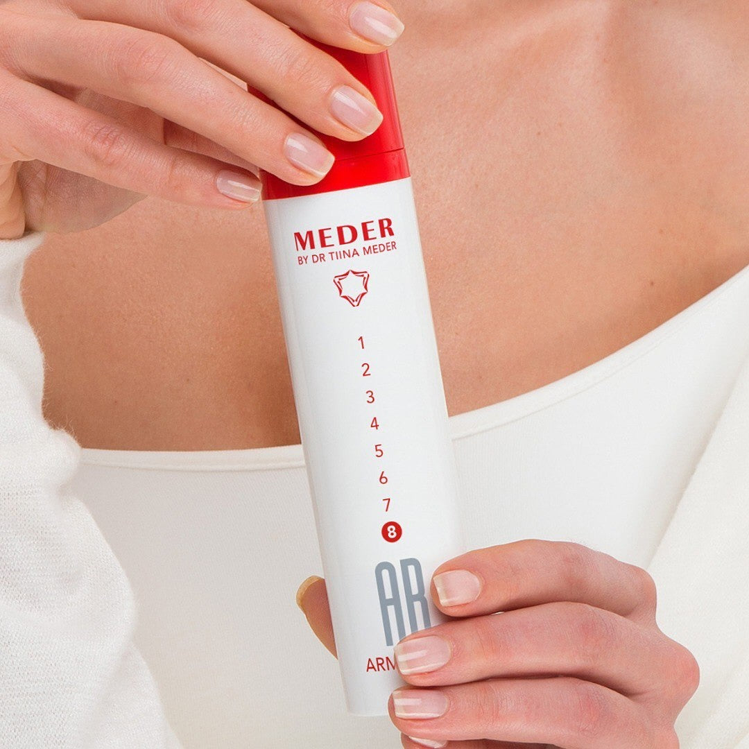 Woman holding the MEDER AB8 Arma-Bust firming cream tube against her décolleté, showing the 1-to-8 dosage scale printed on the tube